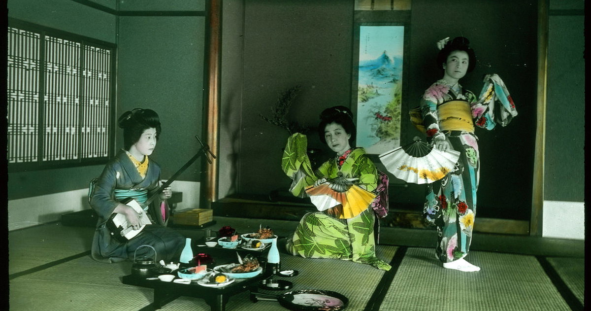 ‘Three women with fans, musical instrument and a table set with food.’ by Herbert Geddes (1908–1918)